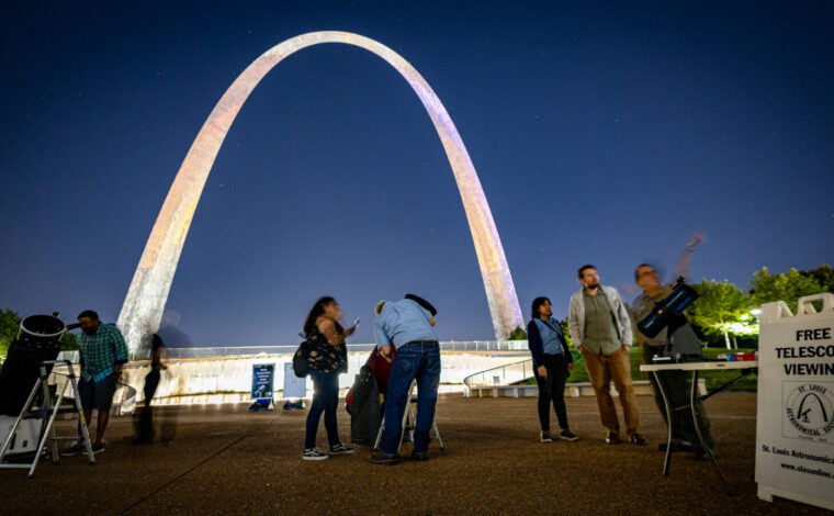 People look into telescopes in front of the Gateway Arch at night during a Gateway to the Stars event